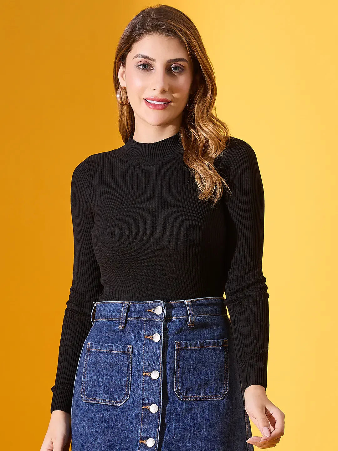 Woman in a 98degreenorth Black Ribbed High-Neck Slim Fit Sweater and blue denim skirt against a yellow background.