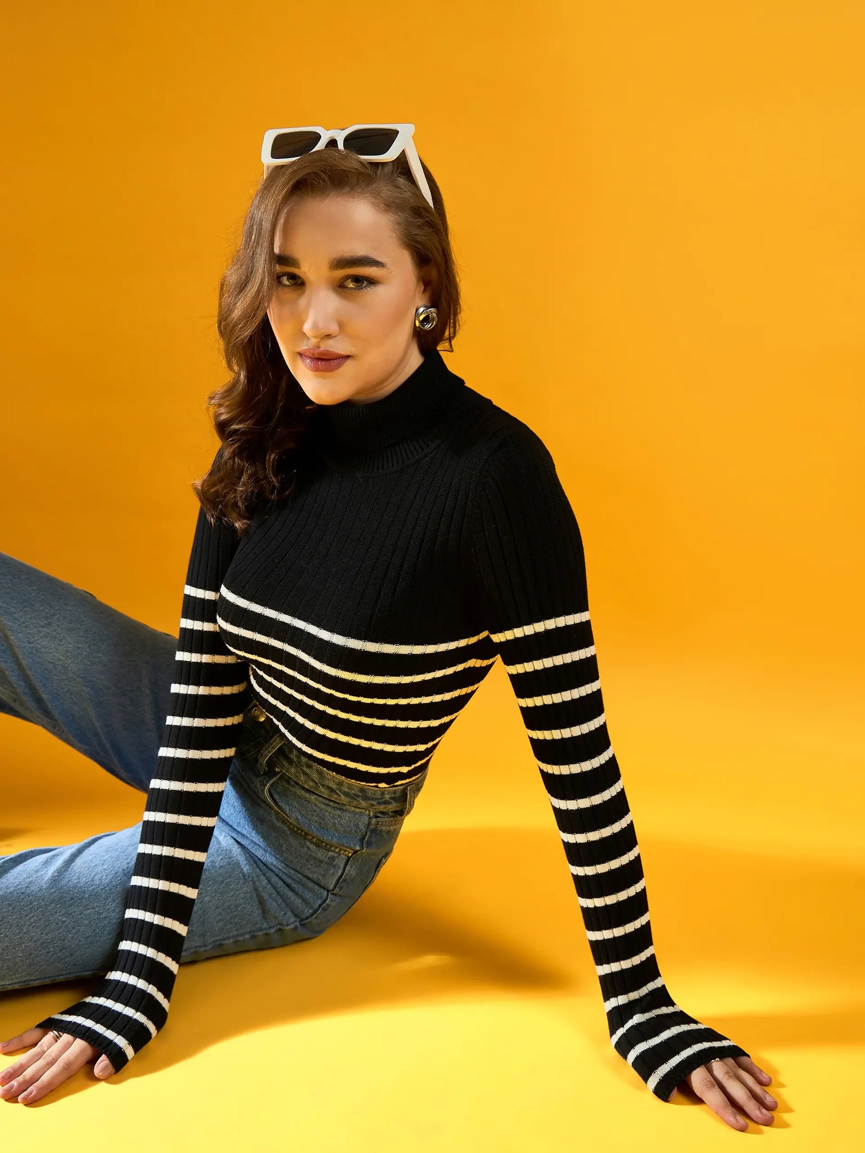 Woman in 98degreenorth Women’s Black Ribbed Striped Turtleneck Sweater and jeans, India, against a yellow background.