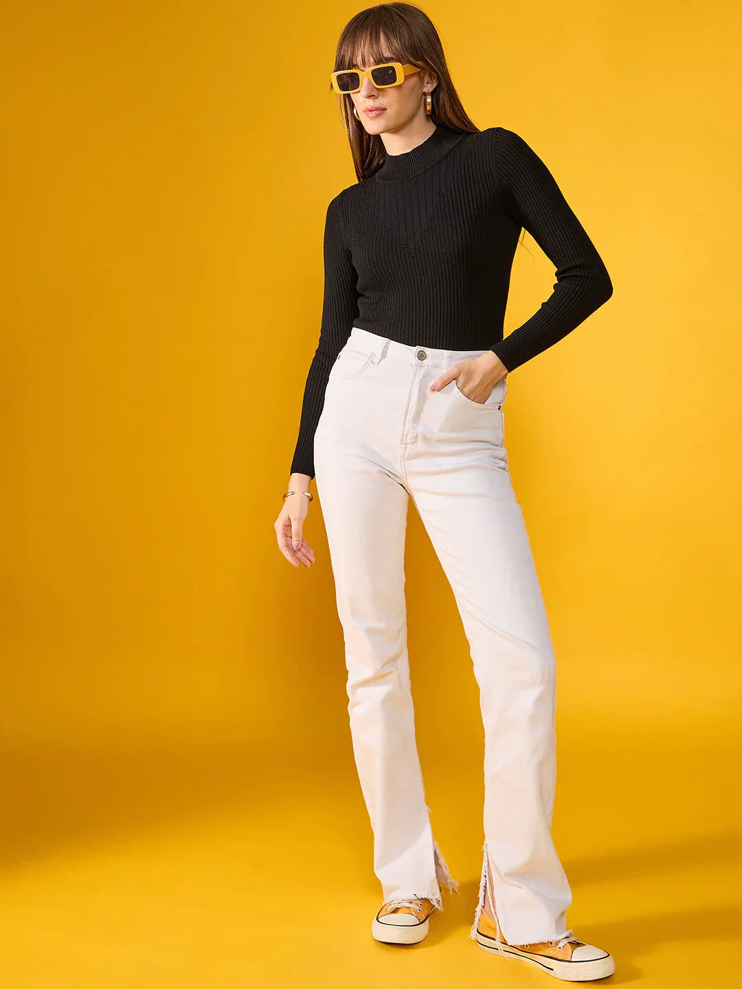 Woman in 98degreenorth black ribbed turtle neck sweater, white pants, and yellow sunglasses on a yellow background.