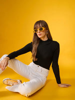 Woman in 98degreenorth Black Ribbed Turtle Neck Sweater poses against a vibrant yellow background.