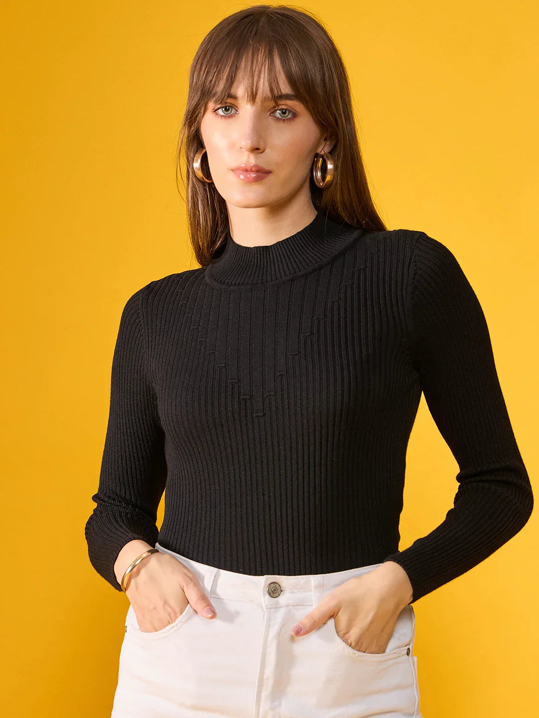 Woman in a 98degreenorth black ribbed slim fit turtleneck sweater stands against a yellow background, facing the camera.