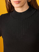 A woman models a 98degreenorth black ribbed slim fit turtleneck sweater and gold hoops against a yellow background.