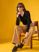 Woman in 98degreenorth black ribbed sweater sits on a chair against a bright yellow background.