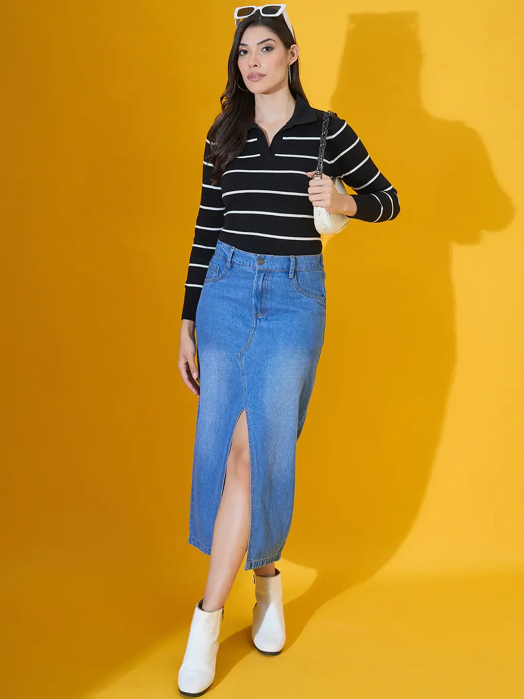 Woman in a 98degreenorth Black Striped Collared Knit Sweater, denim midi skirt, white boots, and sunglasses.