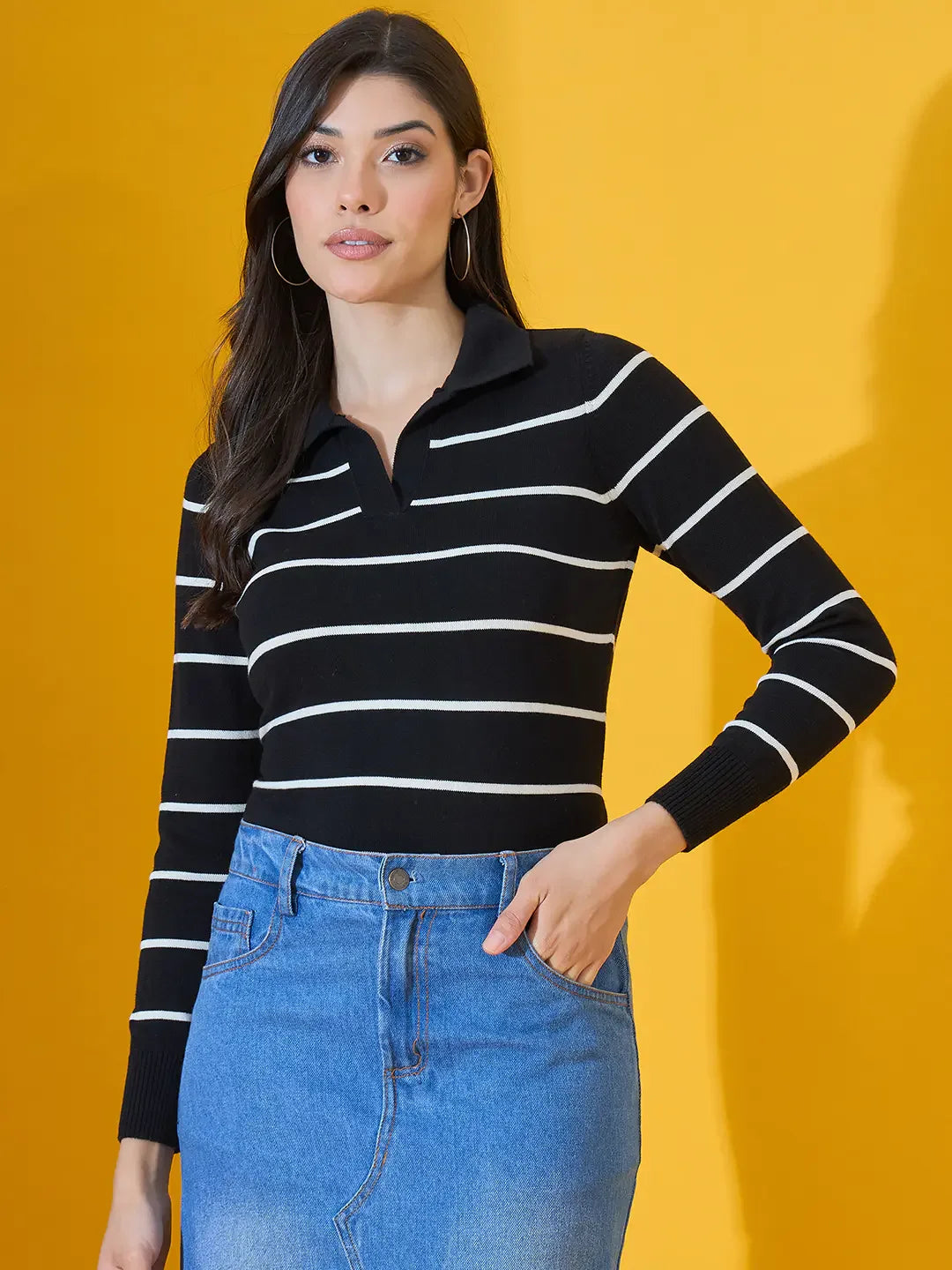 Woman wears 98degreenorth Black Striped Collared Knit Sweater with blue skirt, posing by a yellow background.