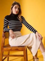 Woman in a 98degreenorth black striped ribbed high neck sweater sits on a wooden chair against a yellow background.