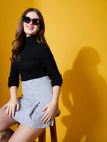 A woman in sunglasses and a 98degreenorth Women’s Black Turtle-Neck Ribbed Sweater sits on a stool by a yellow background.