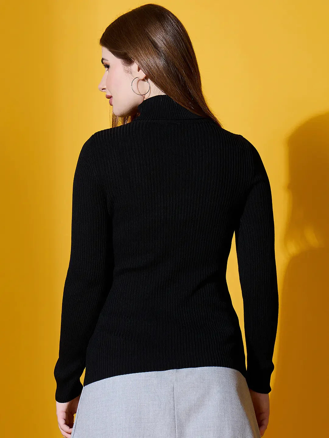 Woman with long brown hair in a 98degreenorth black ribbed turtle-neck sweater, against a yellow background.