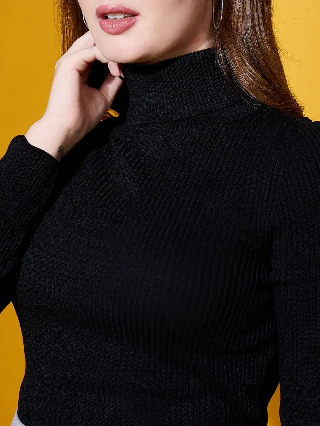 A woman in a 98degreenorth Black Turtle-Neck Ribbed Sweater poses against a yellow background, touching her chin.