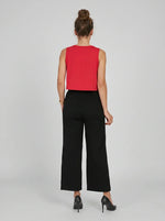 Woman facing away in a sleeveless red top and 98degreenorth black wide-leg high-rise cotton pants on a plain background.