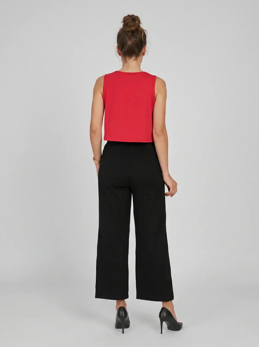 Woman facing away in a sleeveless red top and 98degreenorth black wide-leg high-rise cotton pants on a plain background.