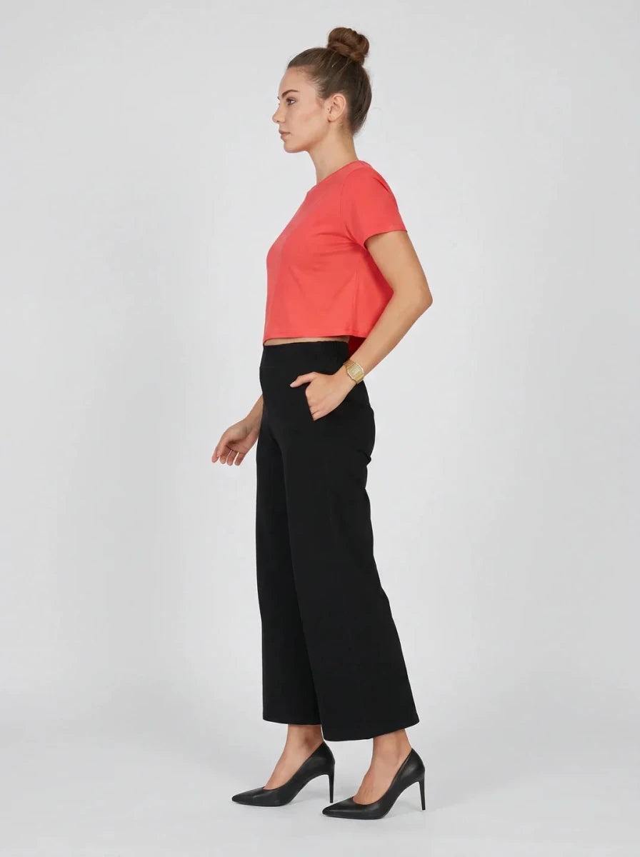 Woman in Women's Black Wide-Leg Cotton Pants by 98degreenorth stands in profile against a plain background.
