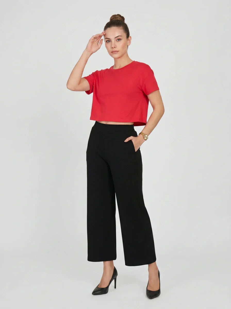 Woman wears 98degreenorth Black Wide-Leg High-Rise Cotton Pants, red crop top, and black heels, hand on head.