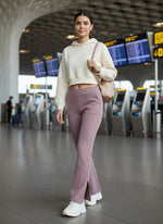 A woman in 98degreenorth Blush Pink Bootcut Sweatpants walks through an airport terminal with check-in kiosks behind her.