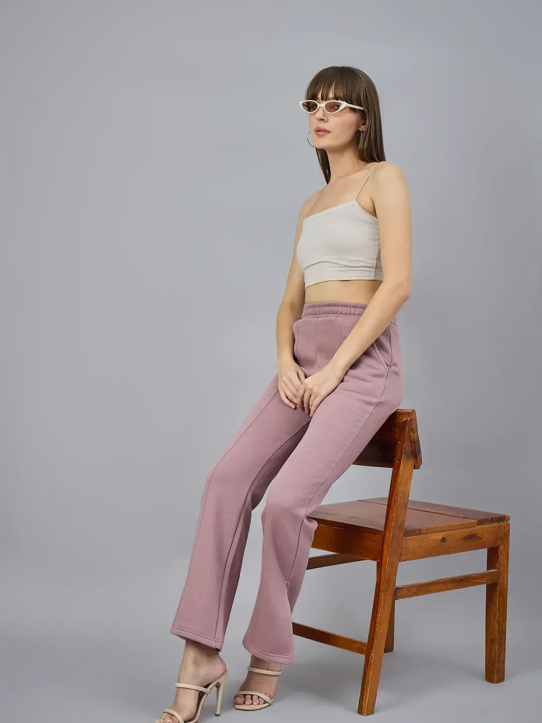 Woman wears 98degreenorth Blush Pink Bootcut Sweatpants, sitting sideways on a wooden chair against a gray background.