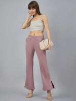 A woman models 98degreenorth Blush Pink Bootcut Sweatpants—flared, side-slit fleece pants—holding a cream clutch.