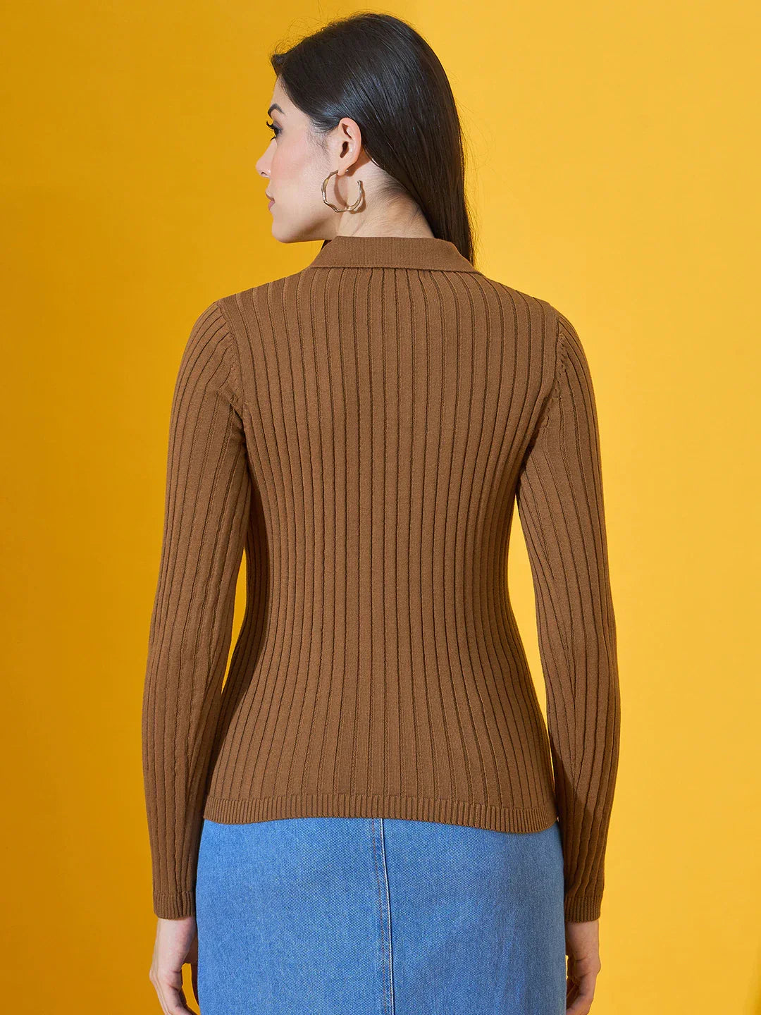 Woman wearing 98degreenorth Women’s Brown Ribbed Collar Neck Sweater and blue denim skirt, facing a yellow background.