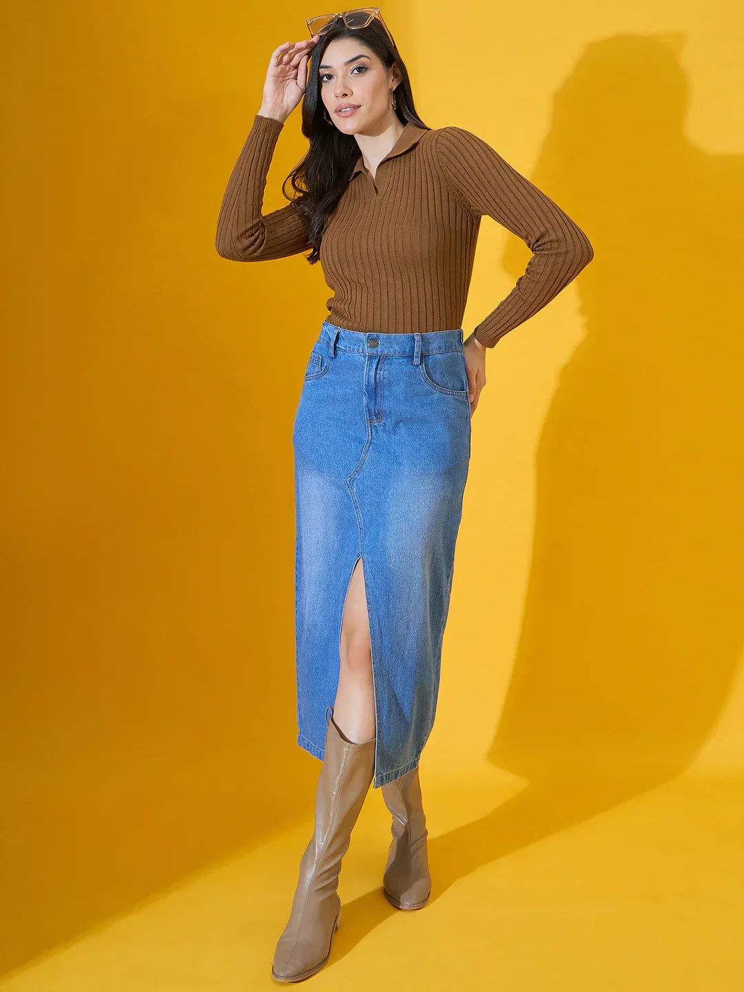 Woman in 98degreenorth slim fit brown ribbed collar sweater and denim skirt poses against a yellow background.