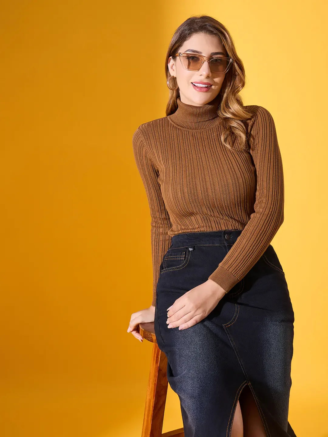 Woman in 98degreenorth’s brown ribbed turtleneck sweater posing against a yellow background.