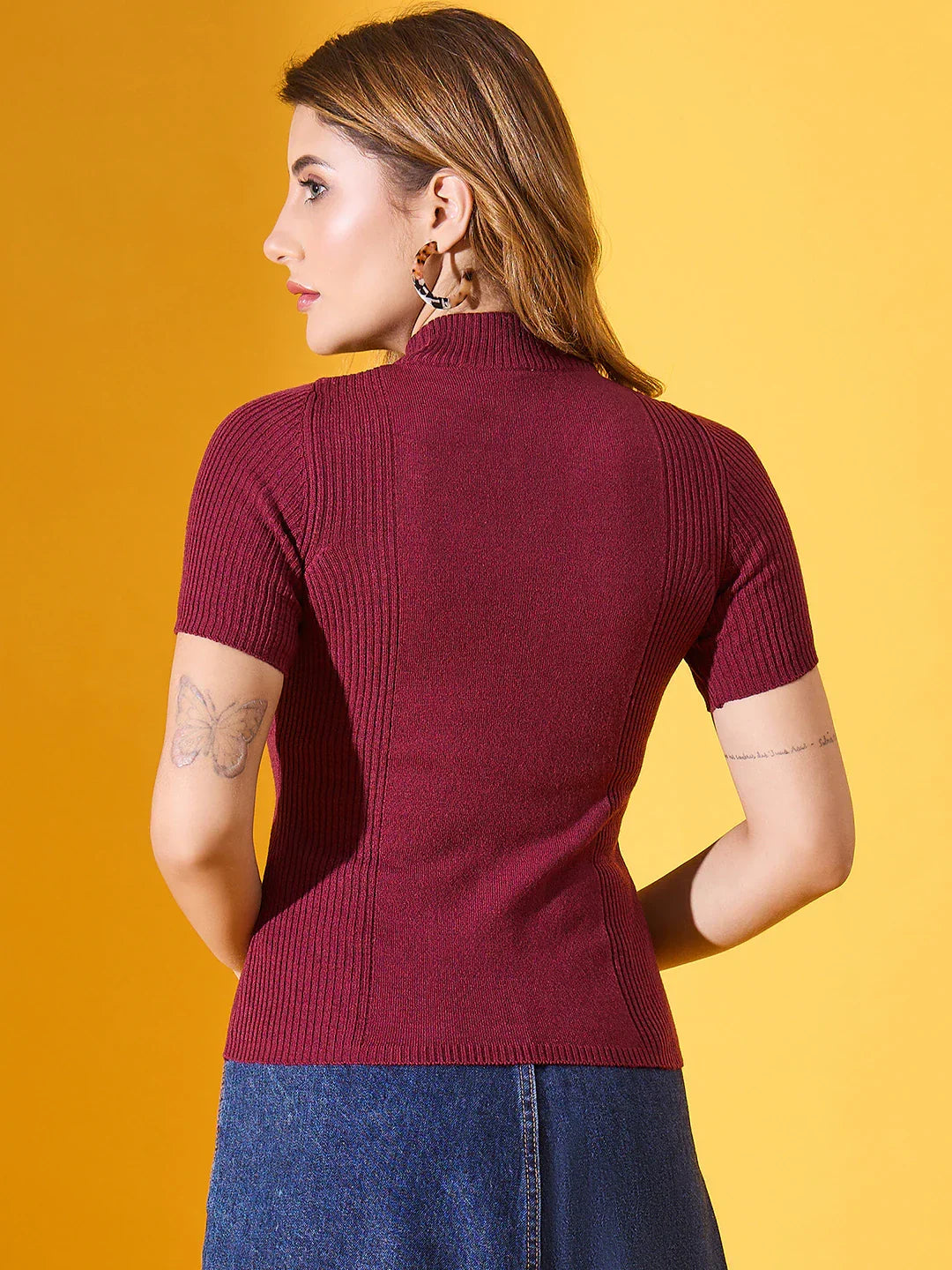 Woman wears 98degreenorth’s burgundy ribbed slim fit turtle neck sweater with a denim skirt against a yellow background.