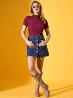 Woman wears 98degreenorth Burgundy Ribbed Turtle Neck Sweater, denim skirt & tan boots against a yellow background.