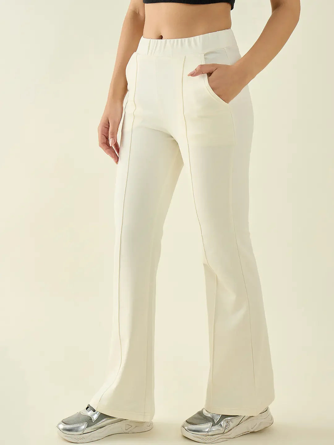 A woman wears 98degreenorth Women’s Butter Flared Bootcut Trousers with a black crop top and silver sneakers.