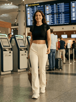 A woman in 98degreenorth Women’s Butter Flared Bootcut Cotton Stretchable Trousers walks through an airport, bag in hand.