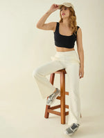 Woman in a black crop top and 98degreenorth Women’s Butter Flared Fit Bootcut Cotton Stretchable Trousers sits on a stool.