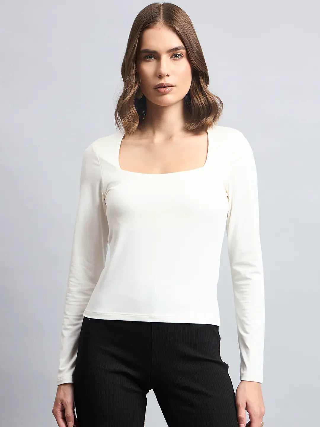 Woman wears 98degreenorth’s Butter Square Neck Long Sleeve Top with black pants, standing against a gray background.