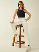 Woman in a black crop top and 98degreenorth Women’s Butter Straight Fit Cotton Trousers sits on a wooden stool.