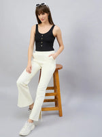 Woman in 98degreenorth butter yellow flared bootcut sweatpants and a black top sits on a stool, wearing sunglasses.