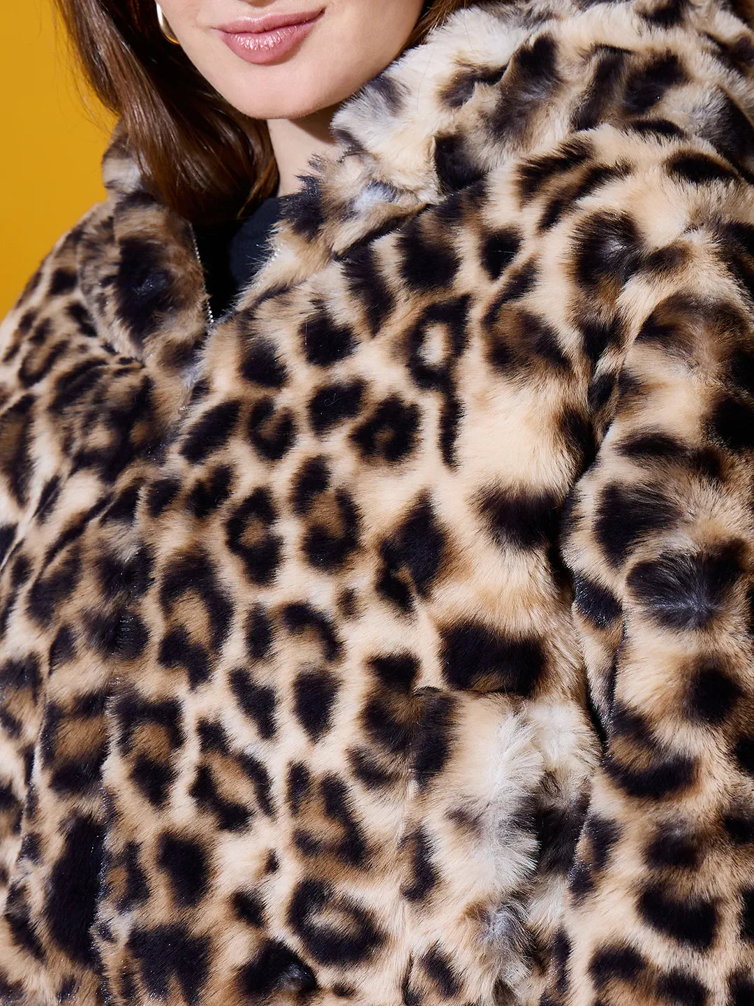 A woman in a 98degreenorth Camel Faux Fur Hooded Jacket stands out against a vibrant yellow background.