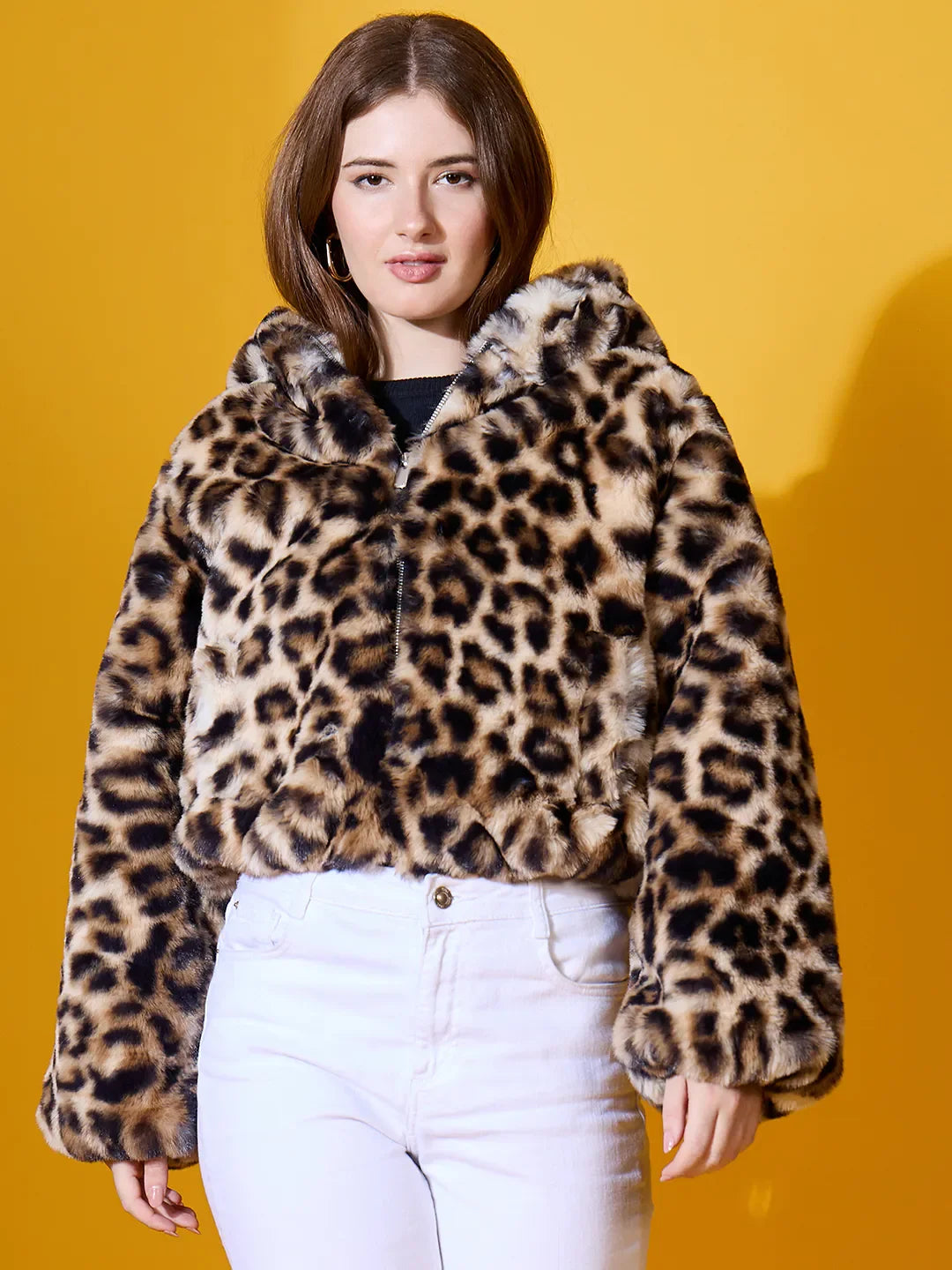A woman models the 98degreenorth Women’s Camel Faux Fur Hooded Jacket, standing stylishly before a bold yellow backdrop.