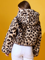 Woman in 98degreenorth’s Camel Faux Fur Hooded Jacket, white pants, facing away on a yellow background.
