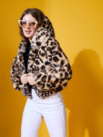 Woman in white pants and black top models 98degreenorth’s Camel Faux Fur Hooded Jacket for city or mountain travel.