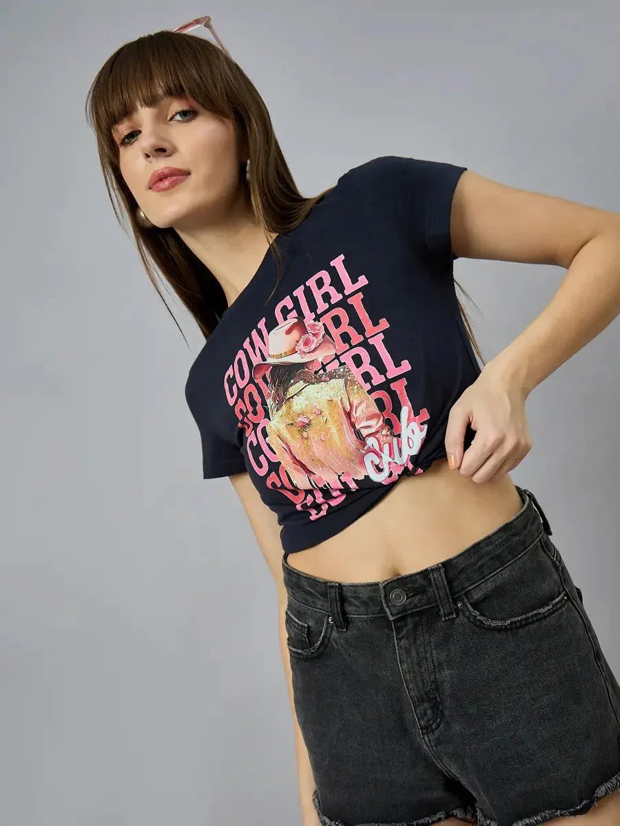 A woman wears a 98degreenorth Women’s casual typography t-shirt in 100% cotton with black shorts, posing by a gray background.