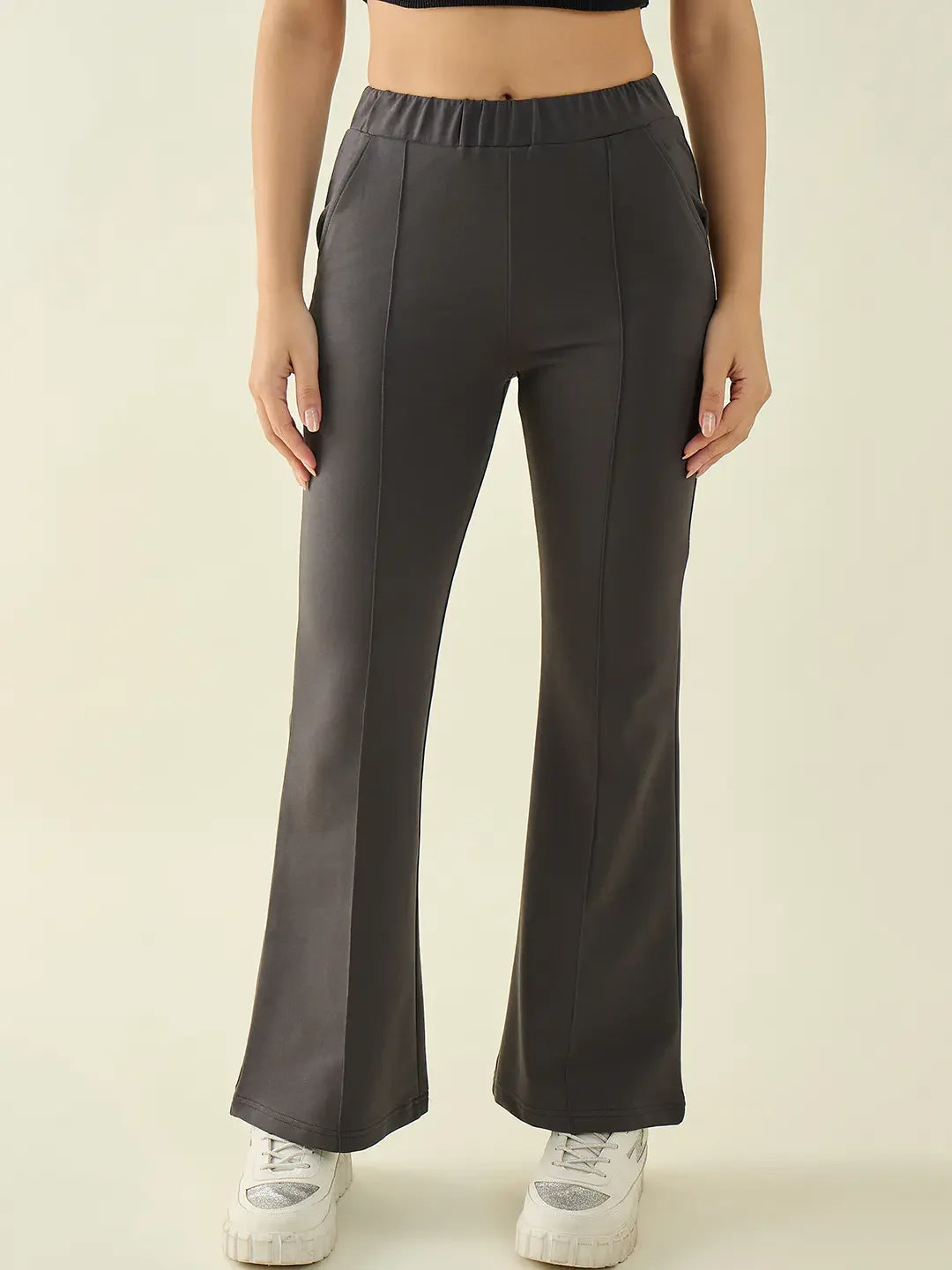 Woman wears 98degreenorth charcoal flared bootcut trousers with a black crop top and white sneakers, facing forward.