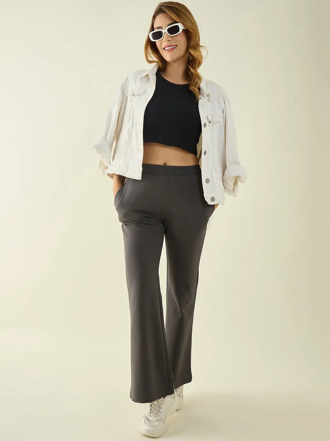 Woman in white jacket and sunglasses, black crop top, and 98degreenorth Charcoal Flared Fit Bootcut Trousers, smiling.