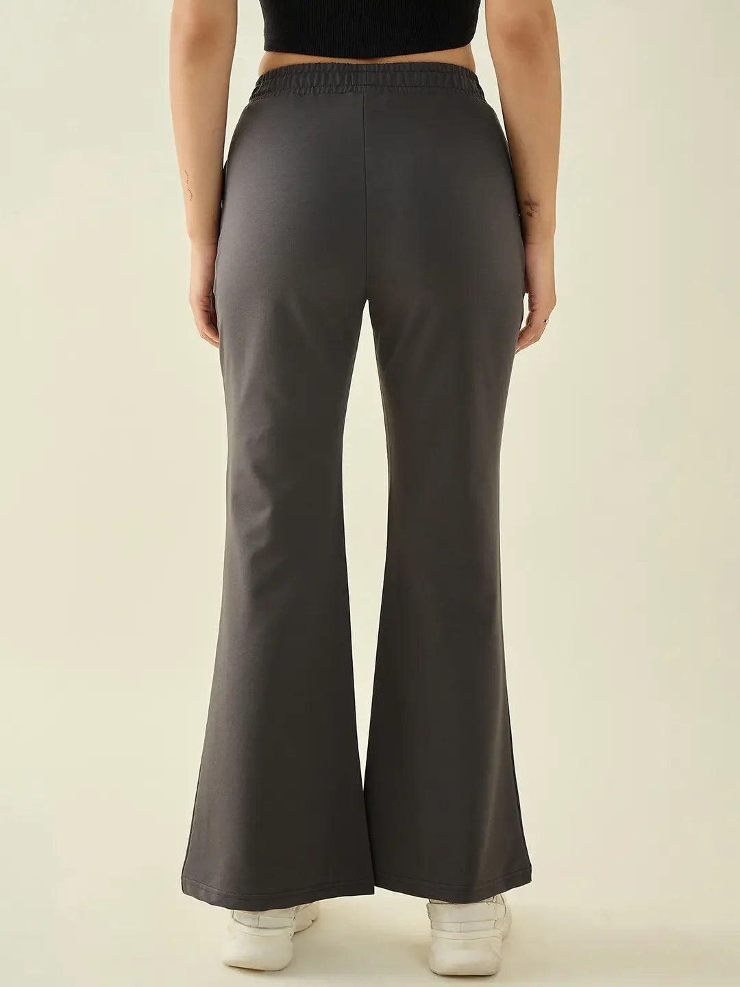 A person in 98degreenorth Women’s Charcoal Flared Fit Bootcut Cotton Trousers and white sneakers, seen from the back.