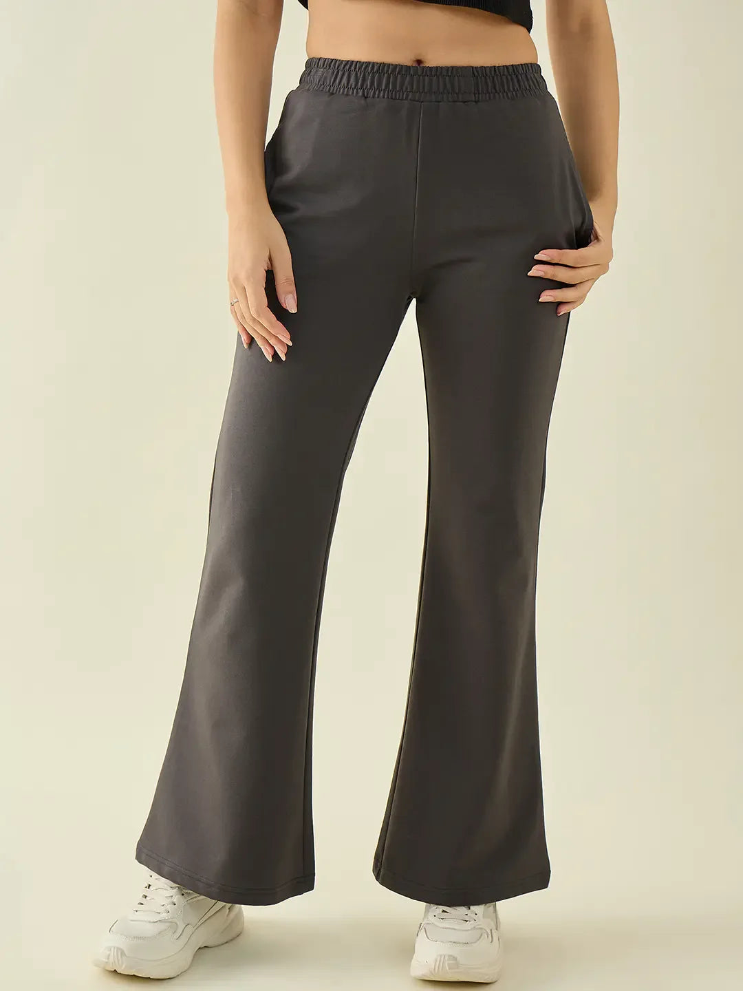 Wearing 98degreenorth Women’s Charcoal Flared Fit Bootcut Trousers, white sneakers, and a black top, hands in pockets.