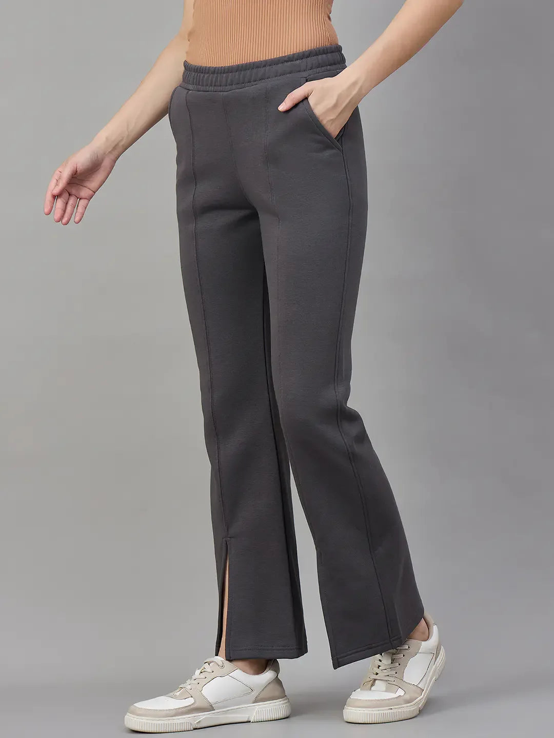 She wears 98degreenorth Women’s Charcoal Grey Bootcut Sweatpants, a beige top, and white sneakers.