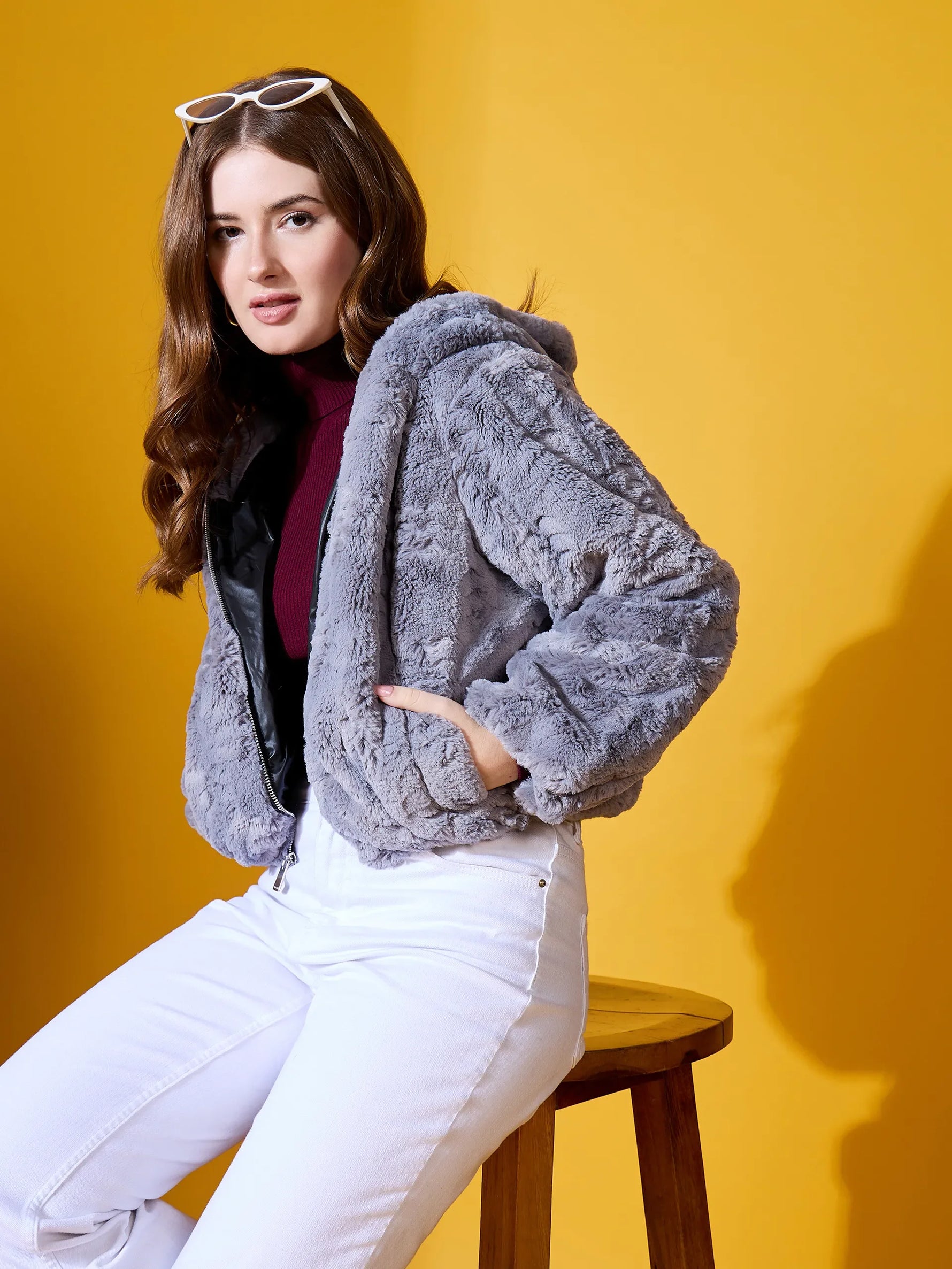 Woman in 98degreenorth Charcoal Grey Faux Fur Jacket poses on stool against yellow background.