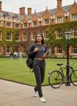 A woman in 98degreenorth Women’s Charcoal Stretchable Trousers walks across campus, books and backpack in hand.