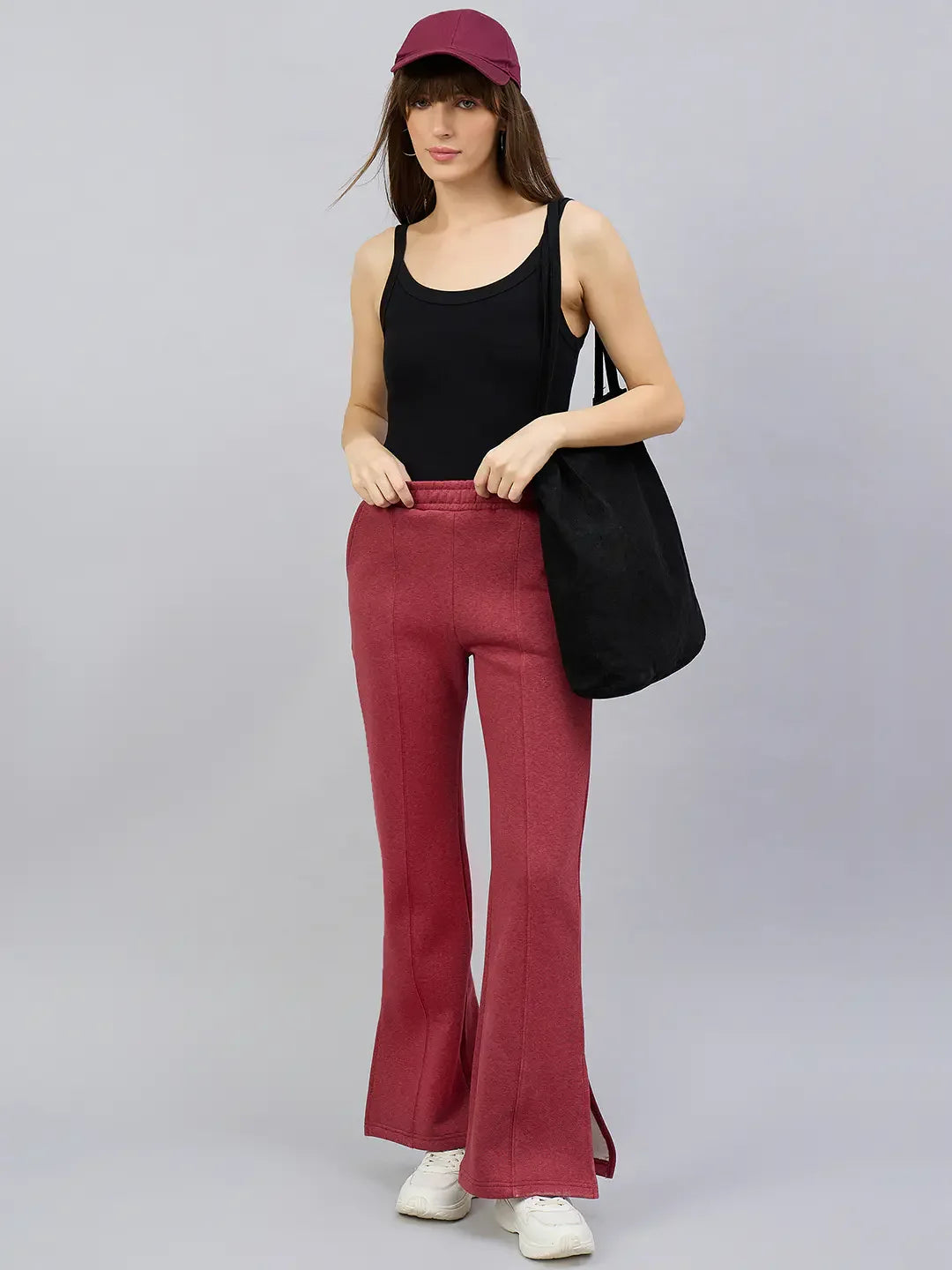 Woman in black tank top and 98degreenorth Cherry Mélange flared lounge pants, cap, sneakers, holding black tote bag.