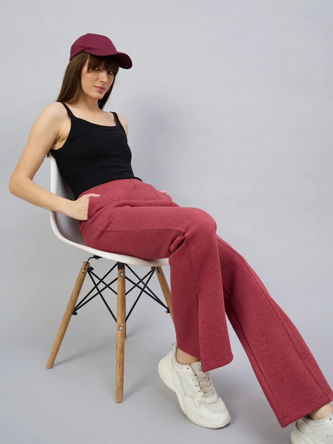 Woman in a black tank top and 98degreenorth cherry mélange bootcut sweatpants sits on a white chair, gray background.