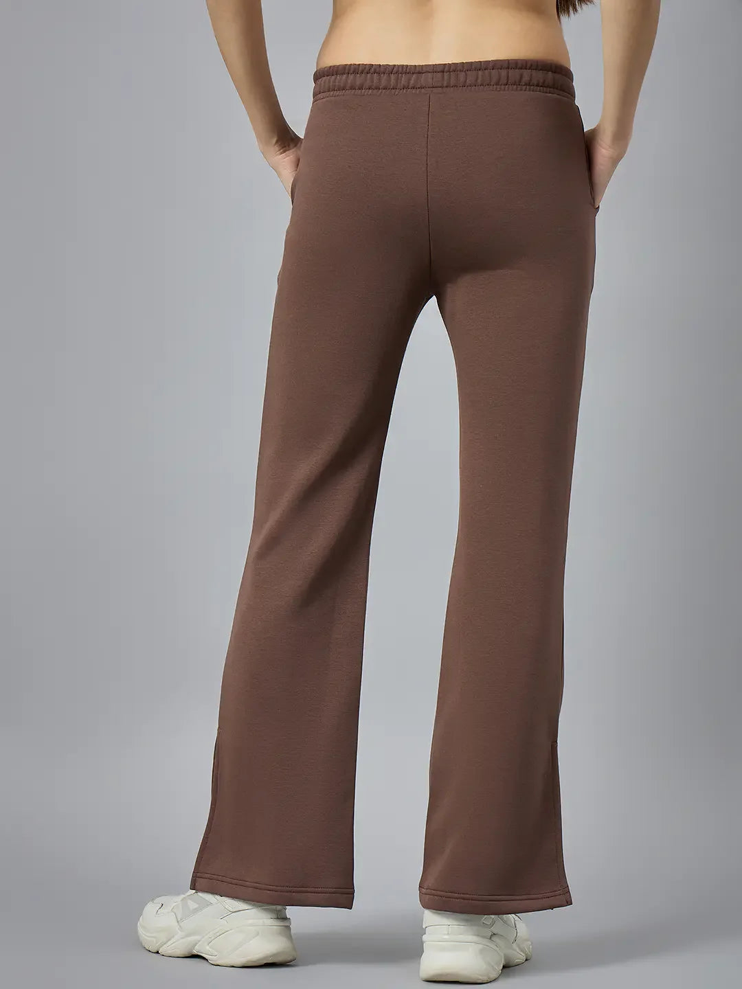 Model wears 98degreenorth Women’s Cocoa Brown Bootcut Sweatpants with white sneakers, hands in pockets, on gray backdrop.