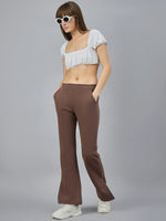 Woman in white crop top and 98degreenorth cocoa brown flared sweatpants stands in white sneakers and sunglasses.