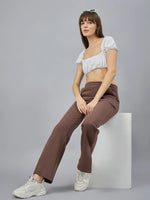 Woman in a white crop top and 98degreenorth Cocoa Brown Bootcut Sweatpants sits on a white block against gray backdrop.