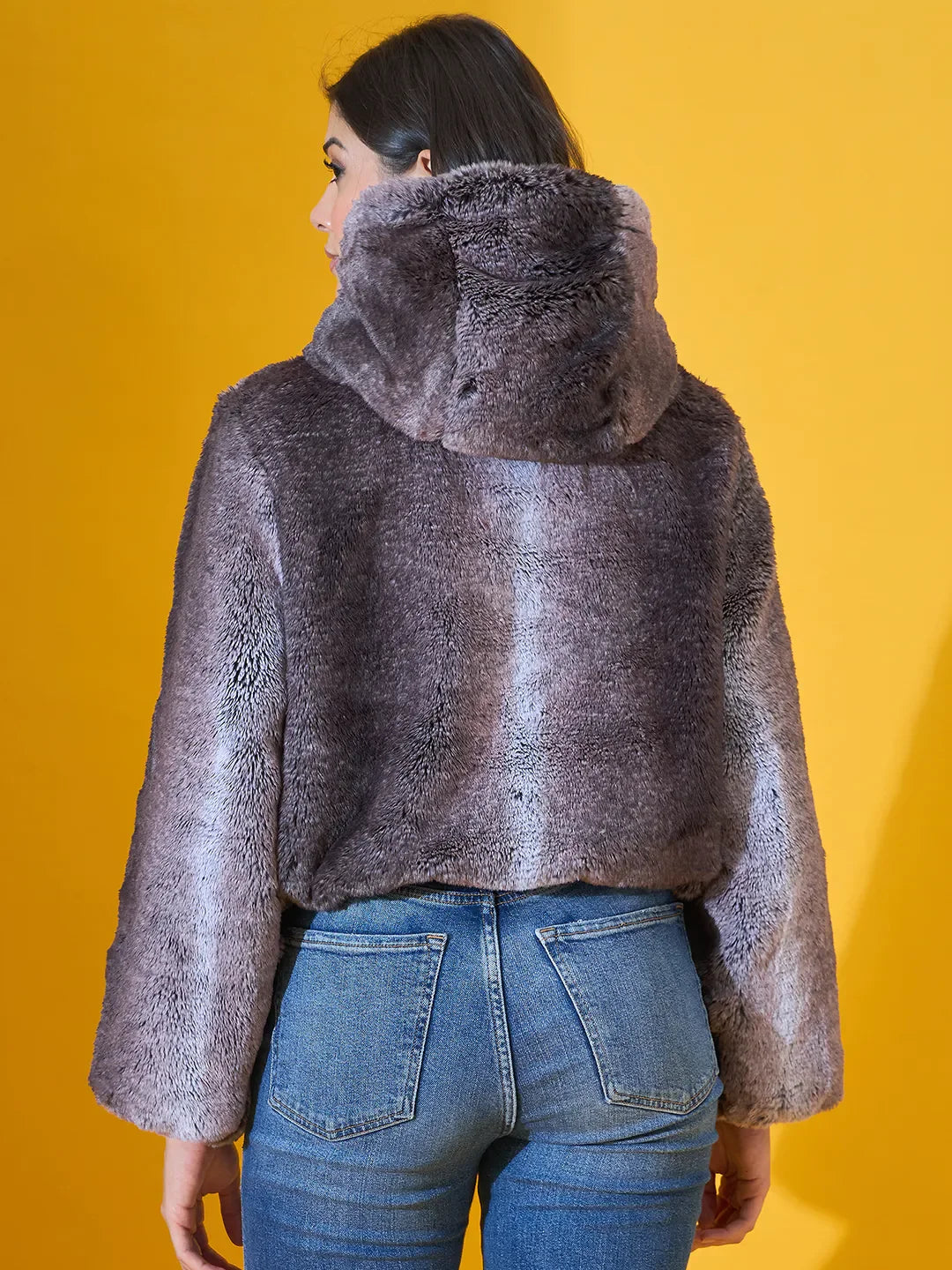 Woman in 98degreenorth coffee brown faux fur jacket, cozy winter layer, against a yellow background.