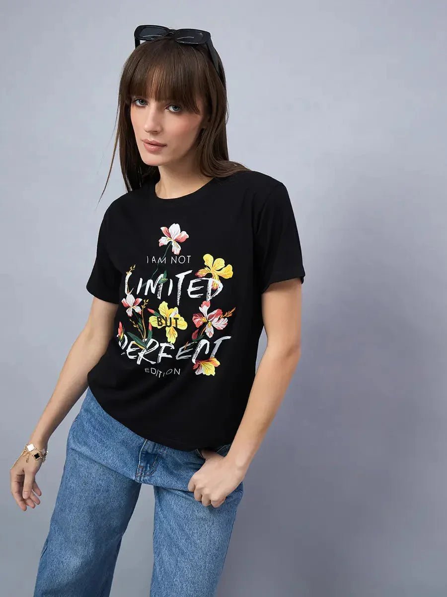 A woman wears a 98degreenorth Women’s Cotton Typography Graphic Tee and blue jeans against a plain gray background.